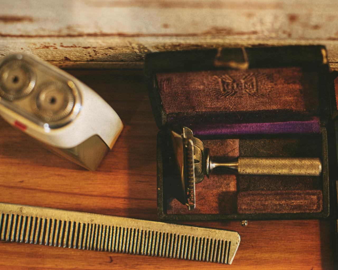 Classic barber tools including a vintage razor and electric shaver on a wooden table.